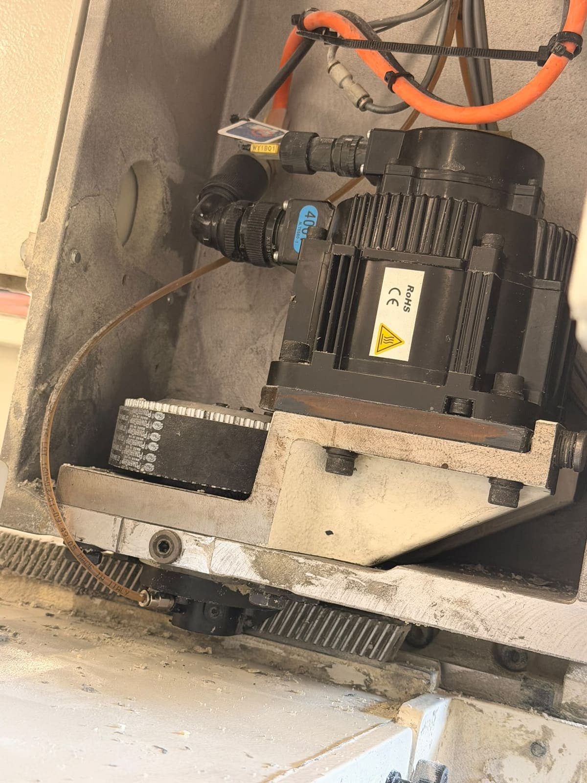 A servo motor and toothed drive belt mounted on a CNC machine axis, orange power cable running to it