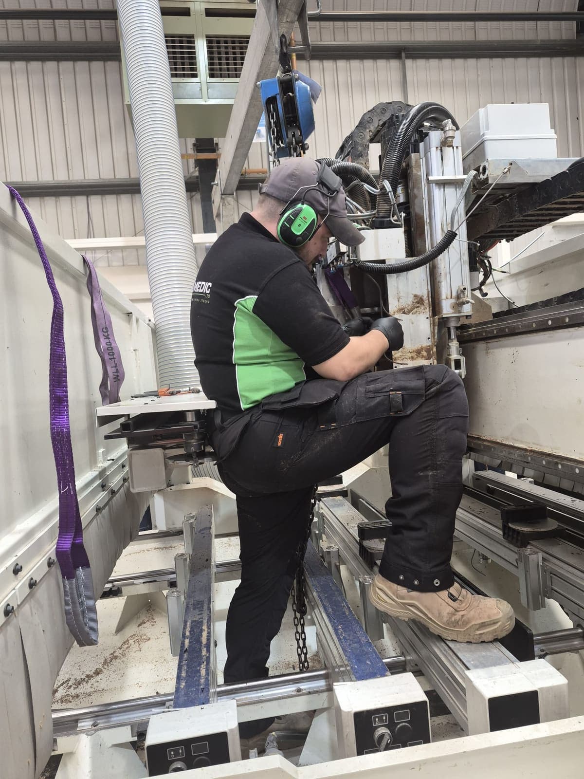Paul Ashall in a black and green CNC Medic polo shirt and ear defenders, working inside the gantry of a CNC machine