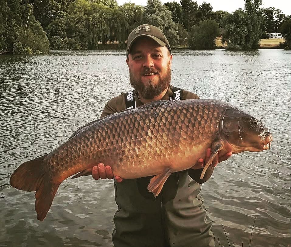 Paul standing in a lake in waders holding a large carp