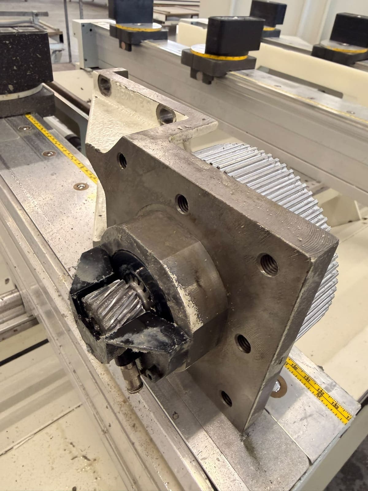 A drive pinion and its mounting plate off a CNC axis, resting on the machine bed with old grease on the teeth
